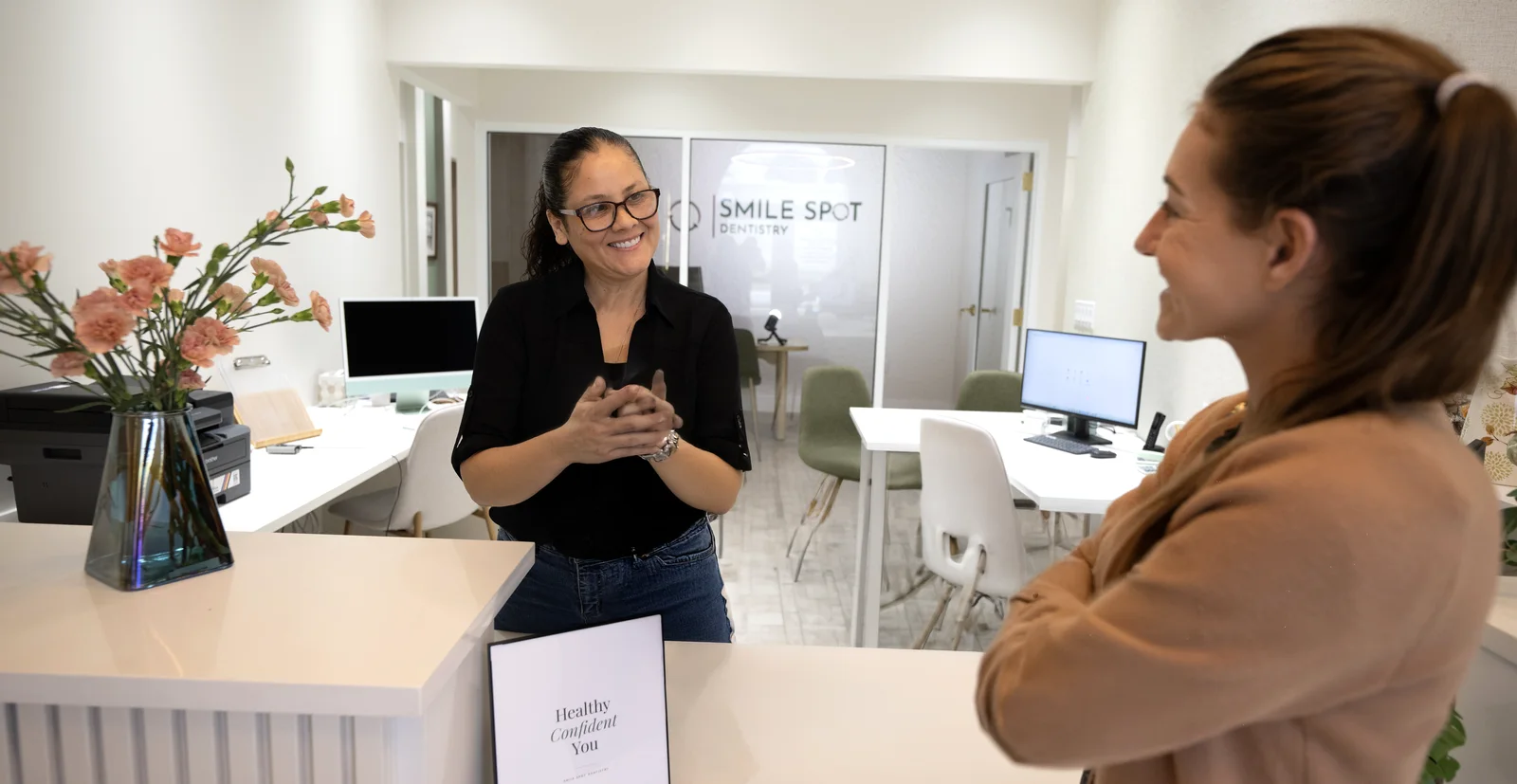 Office manager warmly welcoming a new patient at the front desk — Smile Spot Dentistry, Venice FL